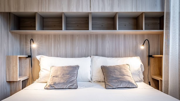 Une chambre à coucher moderne avec une tête de lit en bois, deux lampes de chevet et un lit recouvert de draps blancs et agrémenté de deux oreillers.