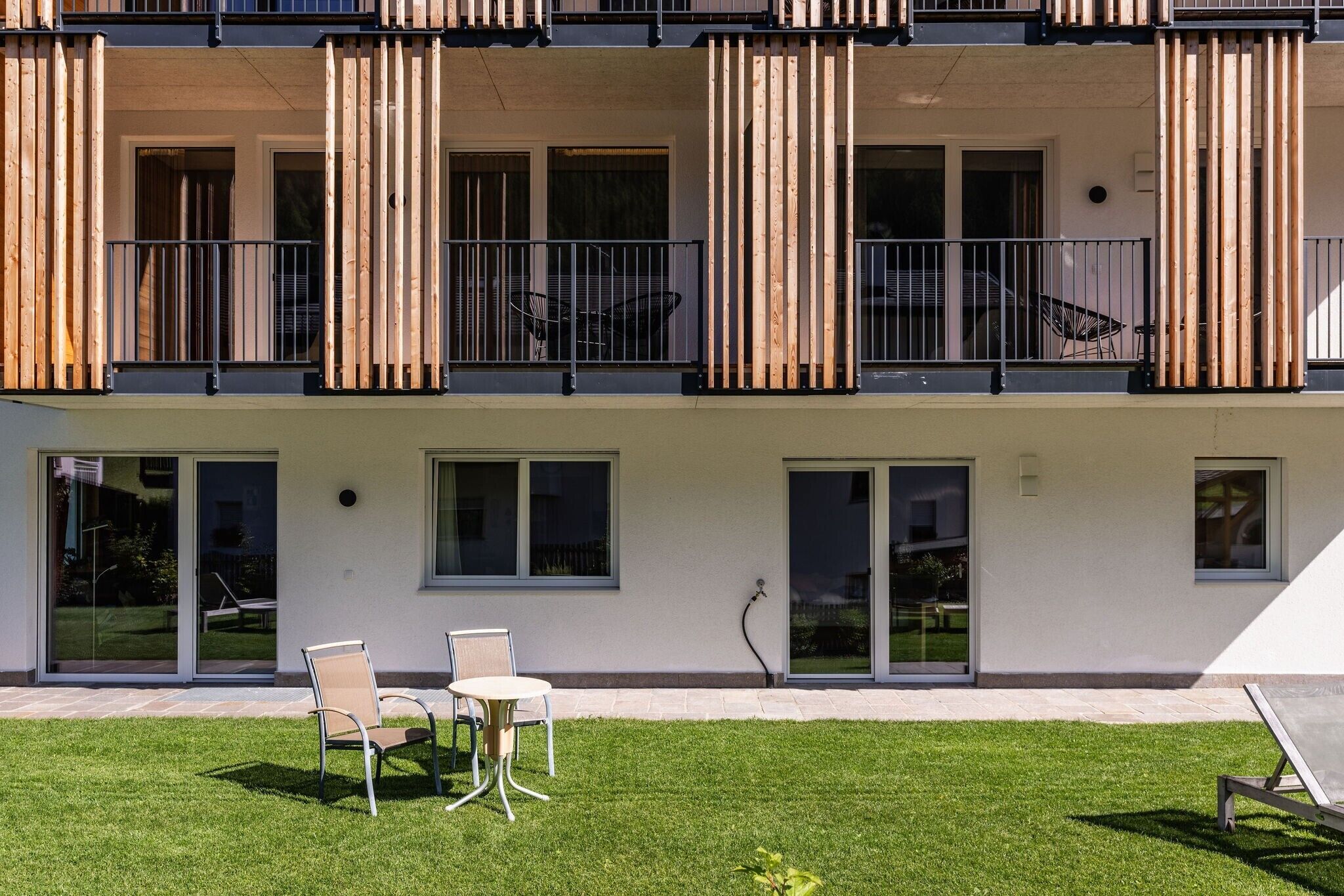 Un edificio moderno con tetto piatto, ampie finestre e un balcone con lamelle di legno verticali.