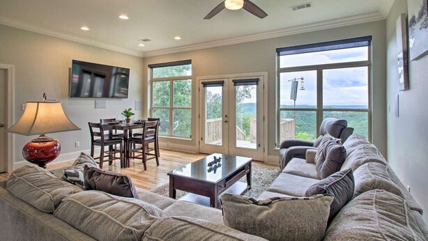 A spacious living room with a ceiling fan, a dining area with a table and chairs, and large windows offering a view of the outdoors.