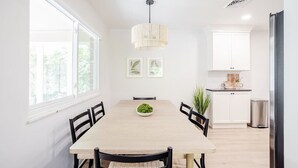 En matplats med ett träbord, svarta stolar, en hängande lampa och inramade tavlor på väggen.