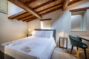 A bedroom with a wooden ceiling, a bed with white linens, a bedside table, a chair, and a mirror on the wall. - YiD Lovely Duomo suite Apt (Firenze)