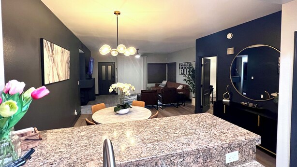A modern kitchen with a granite countertop, a dining area with a round table, and a living room with a brown sofa. - Condominium close to New Raider’s stadium, Strip, restaurants and attractions.  (Las Vegas)