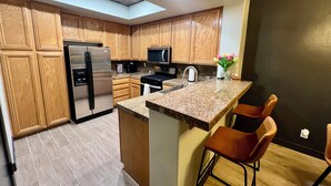 A modern kitchen with wooden cabinets, a stainless steel refrigerator, a microwave, and a granite countertop. - Condominium close to New Raider’s stadium, Strip, restaurants and attractions.  (Las Vegas)