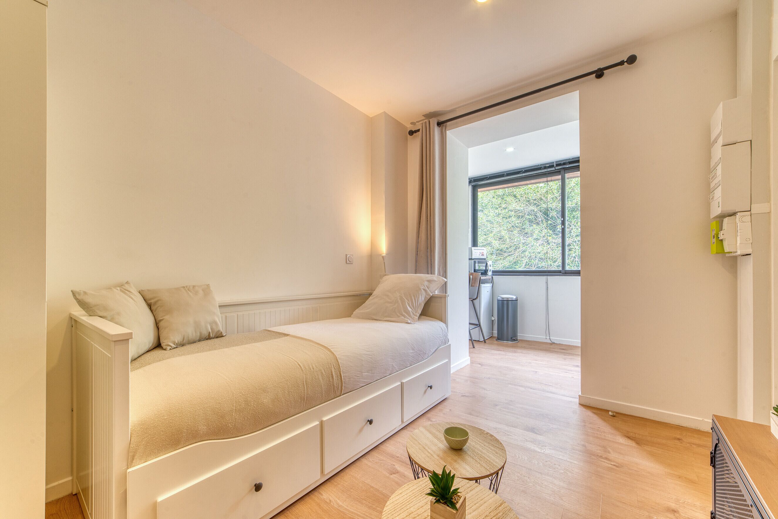 A modern bedroom with a bed, bedside tables, and a view of the outdoors.