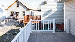 Une terrasse en bois avec des balustrades blanches, qui mène à un bâtiment blanc doté d’un toit brun.