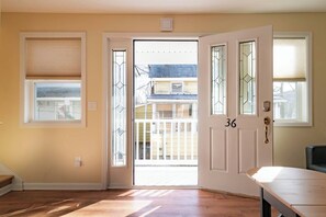 Une pièce avec un plancher en bois, une porte blanche portant un numéro et une fenêtre avec des stores.