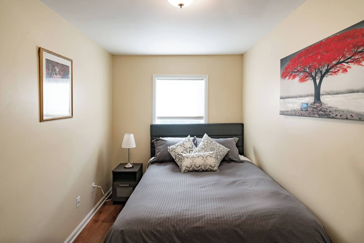 A bedroom with a bed, a nightstand, a window, and a painting on the wall.