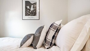 Un lit avec une literie blanche et trois oreillers aux motifs différents.