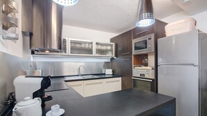Een moderne keuken met een zwart aanrecht, roestvrijstalen apparatuur en een gele stoel.
