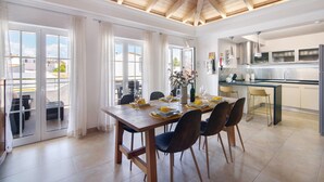 Een eethoek met een houten tafel, stoelen en uitzicht door glazen deuren naar buiten.