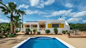 Una casa con piscina, palmeras y un cielo azul despejado.