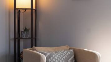 Ett hörnrum med en beige fåtölj, en golvlampa och en tavla som hänger på väggen.