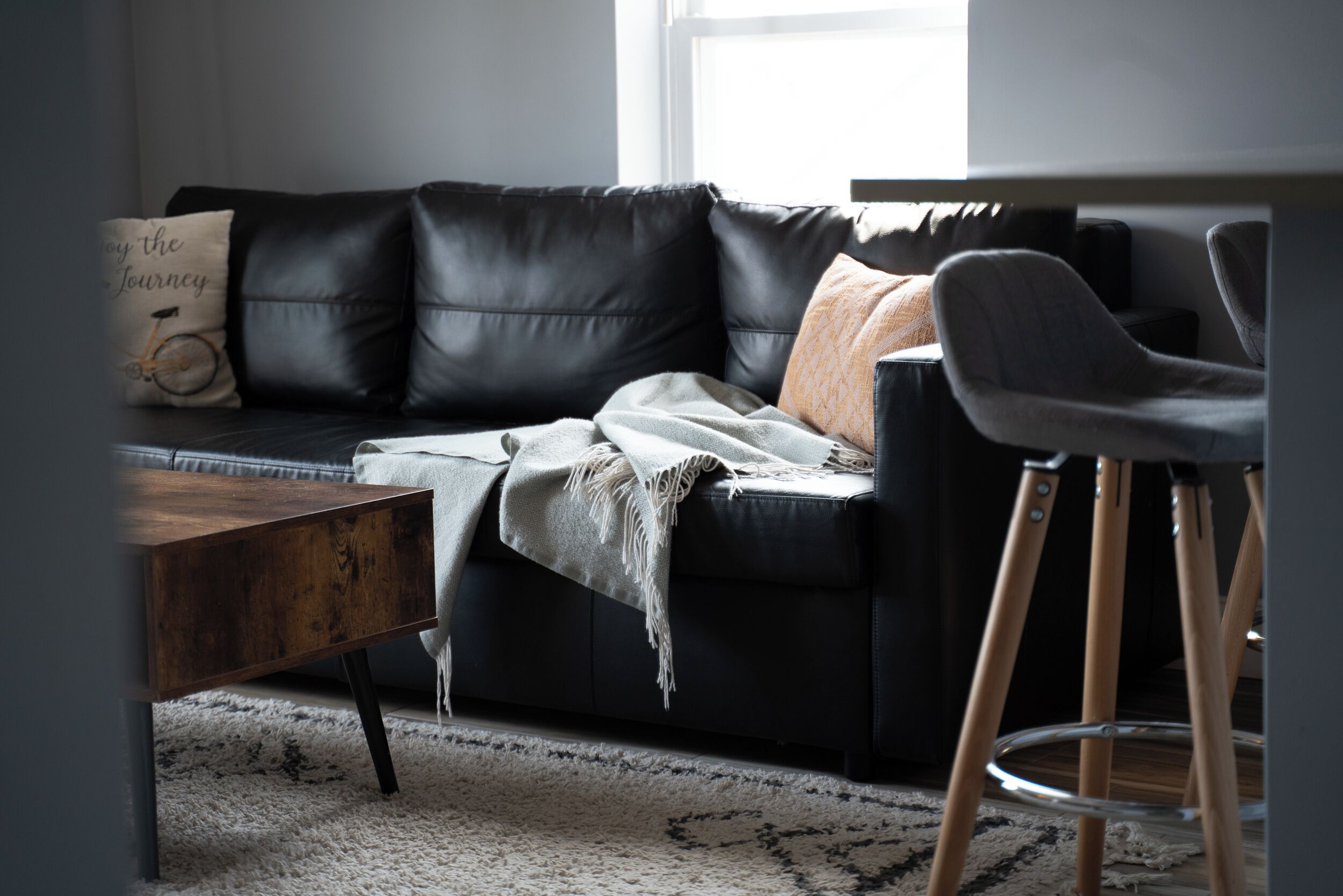 Un salon moderne avec un canapé en cuir noir, une table basse en bois et un tabouret de bar.