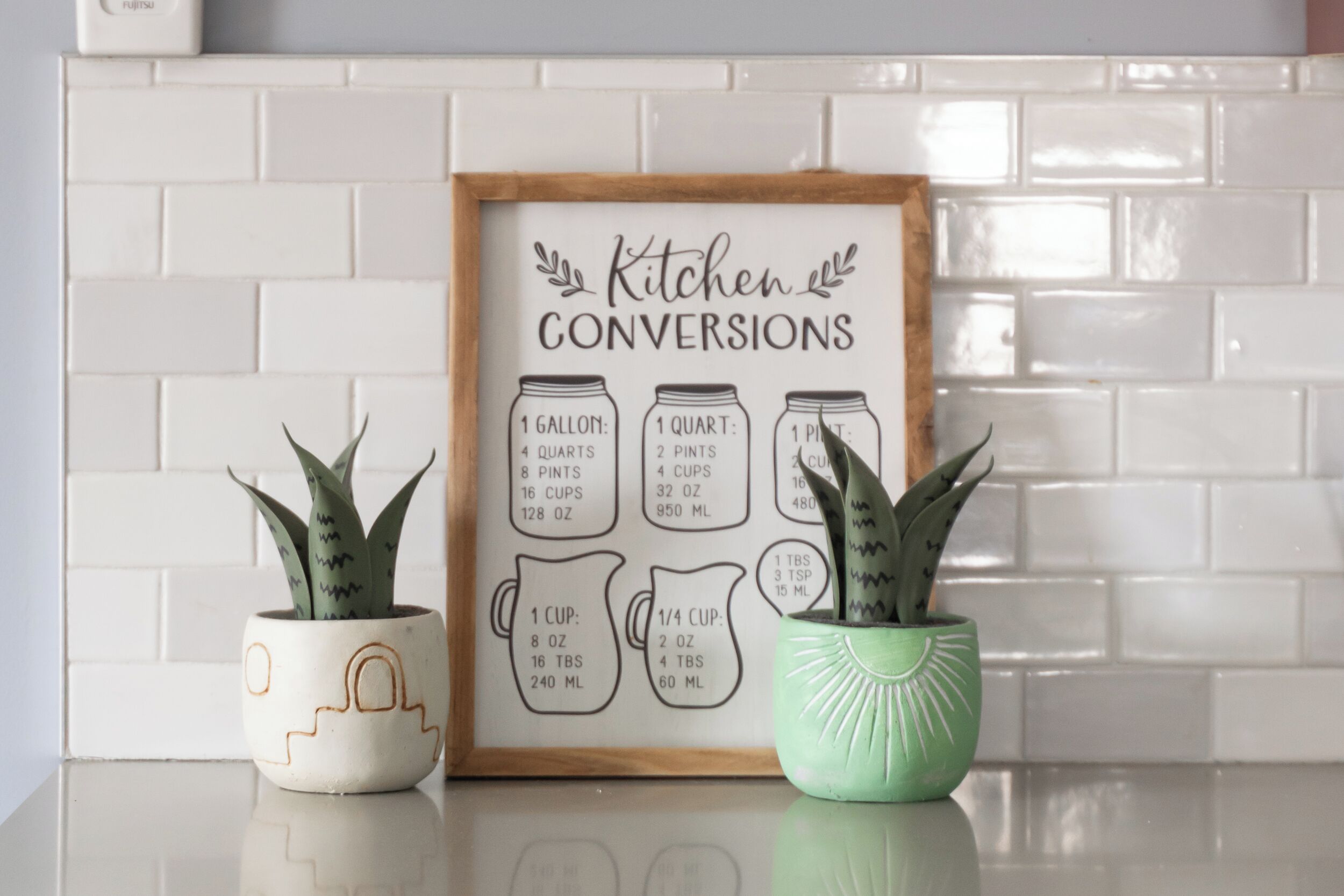A framed kitchen conversions chart with potted plants on either side.
