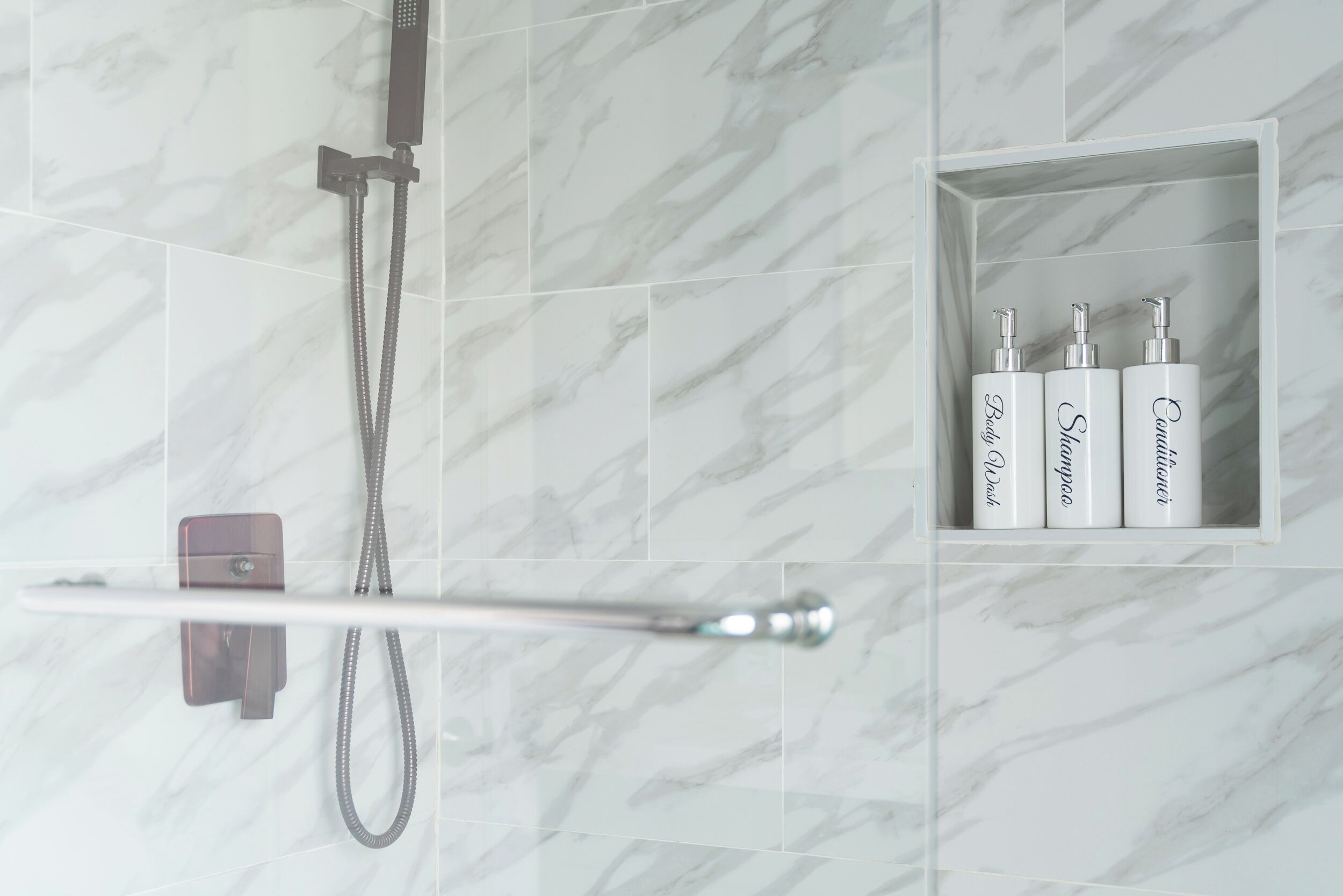 Ein Badezimmer mit Dusche, Handtuchhalter und Ablagefläche mit drei Shampooflaschen und Conditioner.
