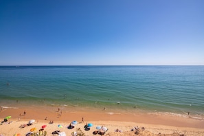 Ein Strand mit badenden und sonnenbadenden Personen sowie Sonnenschirmen im Sand.