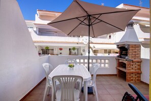 Une terrasse avec une table et des chaises, un four en briques et une clôture blanche.