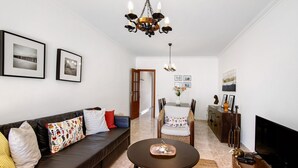 Ein Wohnzimmer mit braunem Sofa, einem runden Couchtisch, einem Fernseher und einer Deckenleuchte.