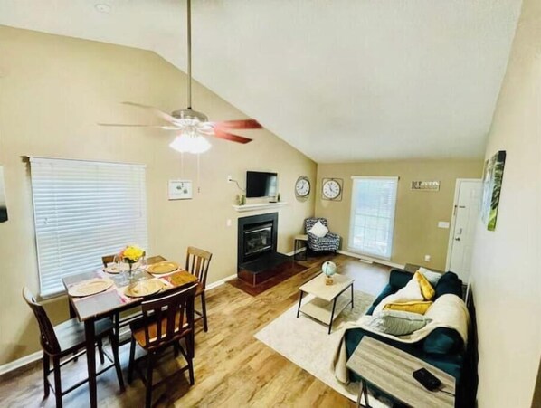 Cozy living space with a fireplace, dining area, and seating area, featuring a TV and ceiling fan.