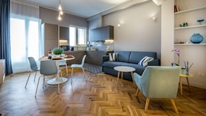 A modern living room with a sofa, chairs, a dining table, and a kitchen area. - Apartments Florence - Cobalt Cove 2bdr (Florence)