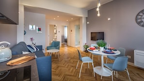 A modern living room with a sofa, dining table, and chairs. There is a television mounted on the wall and a clock. - Apartments Florence - Cobalt Cove 2bdr (Florence)