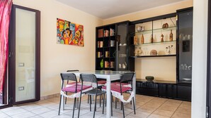 A dining area with a glass table, four chairs, a bookshelf, and a decorative shelf with pottery. - Holiday Home 'Magy House' with Private Terrace (Quartu Sant'elena)