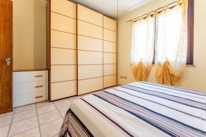 Un dormitorio con cama, armario y ventana con cortinas.