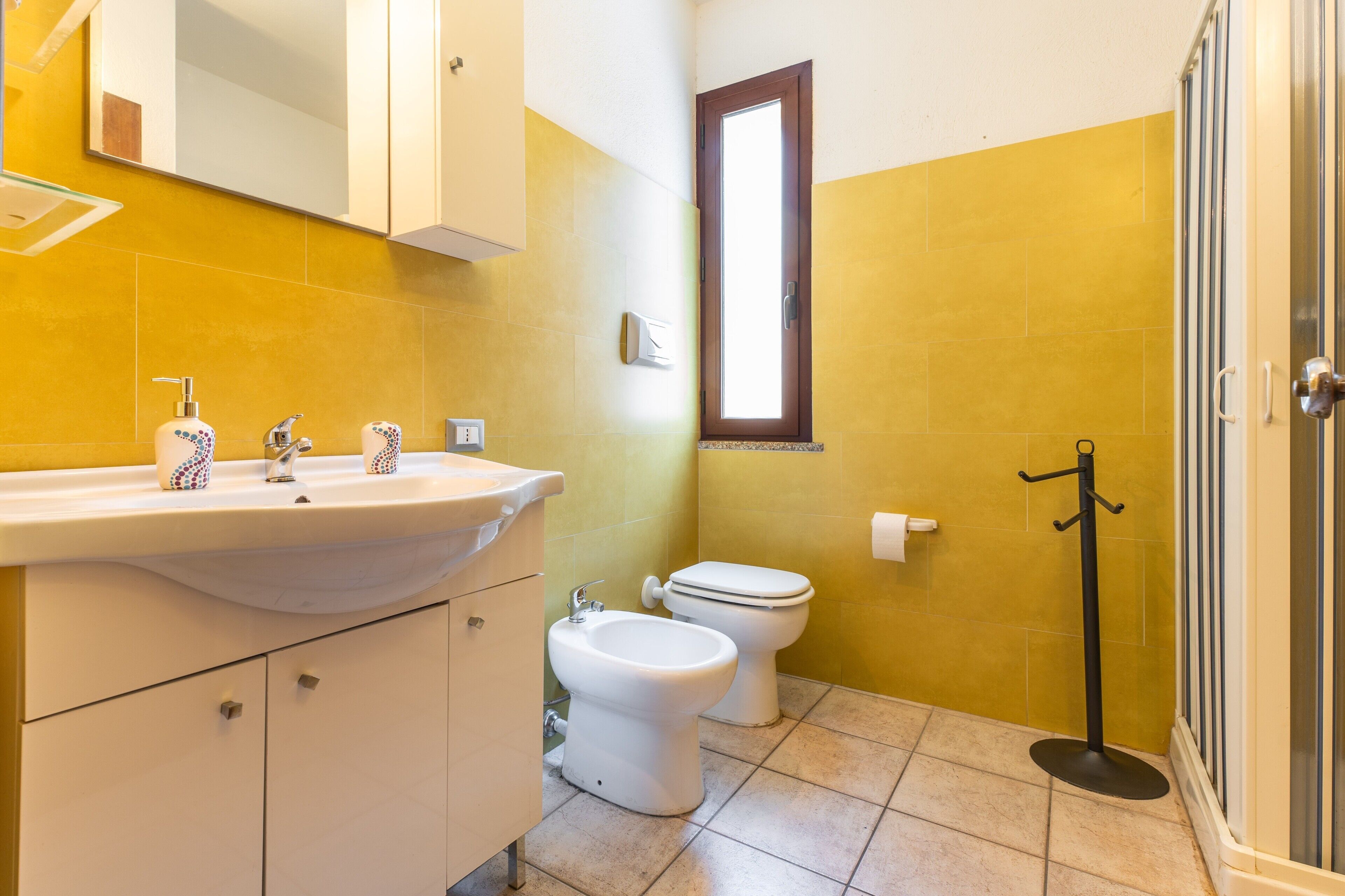 Ein Badezimmer mit Waschbecken, zwei Toiletten, einem Bidet, einem Spiegel und einem Handtuchhalter.