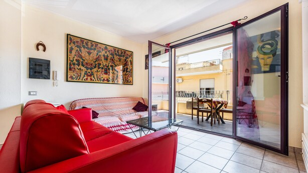 A living room with a red sofa, a glass table, a patterned sofa, and a large painting on the wall. - Holiday Home 'Magy House' with Private Terrace (Quartu Sant'elena)