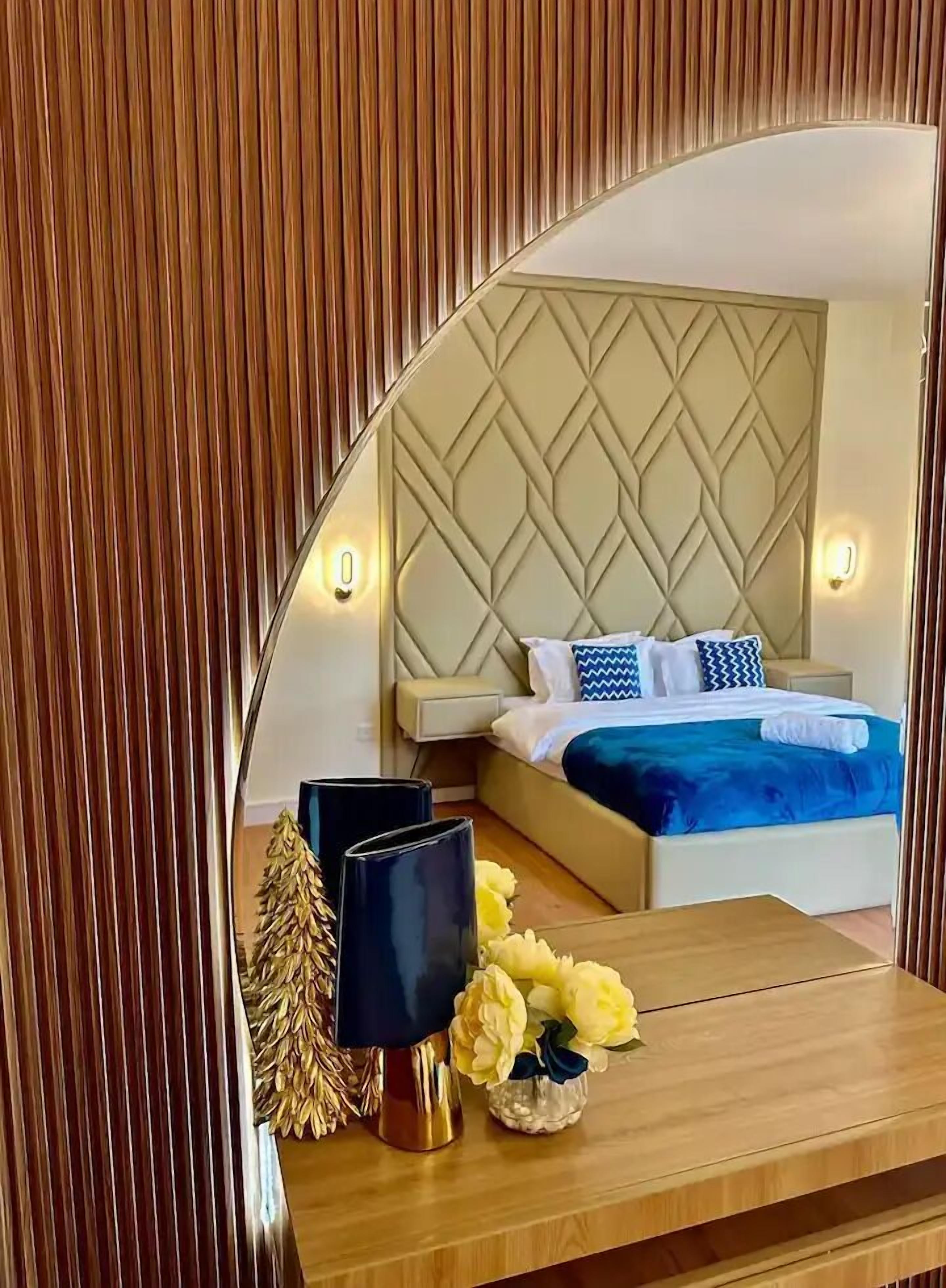 A bedroom with a bed, bedside tables, and a mirror reflecting the room.