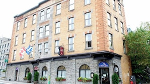 Un hôtel à plusieurs étages, doté d’une façade en pierre, de nombreuses fenêtres et d’une enseigne « Le Blues Café » au niveau du rez-de-chaussée.
