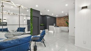Un hall d'hôtel moderne avec un comptoir d'accueil, un espace salon avec des chaises bleues, un mur végétal et un mur décoratif en briques.