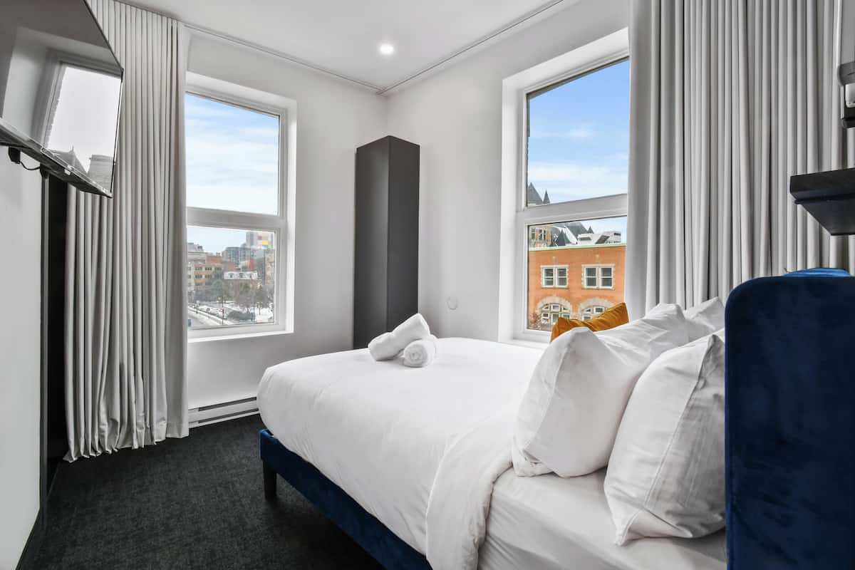 A hotel room with a large bed, a view of buildings, and a window with curtains.
