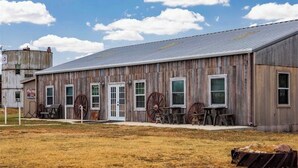 A rustic wooden building with large windows and a metal roof, featuring a small outdoor seating area with wooden tables and chairs.