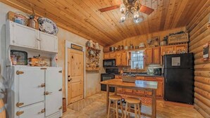 A rustic kitchen with wooden cabinets, a white refrigerator, a black stove, and a dining table with stools.