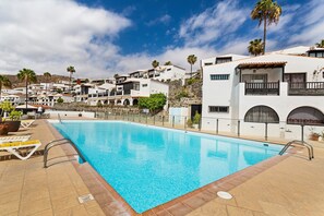 En swimmingpool med solstolar, en stenmur och vita byggnader med balkonger.