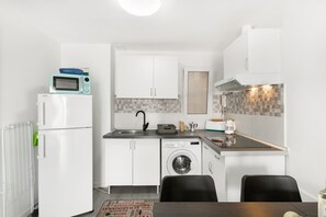 A compact kitchen with a refrigerator, microwave, washing machine, sink, and a dining area with chairs. - Holiday Apartment 'Bungalow Josephin' with Shared Pool, Private Terrace and Wi-Fi (Patalavaca)