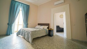 A bedroom with a bed, a nightstand, a door leading to another room, and a window with curtains.