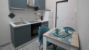 A compact kitchen with a sink, stove, and a small refrigerator. There is a dining table with chairs and a tray with cups and a plate.