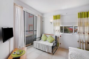 Quarto com uma cama, televisão, mesa com telefone e controle remoto, janela com cortinas e porta deslizante.