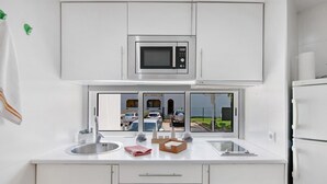 Eine moderne Küche mit eingebauter Mikrowelle, einem Fenster mit Blick auf parkende Autos und ein Gebäude, ein Spülbecken und ein Kühlschrank.