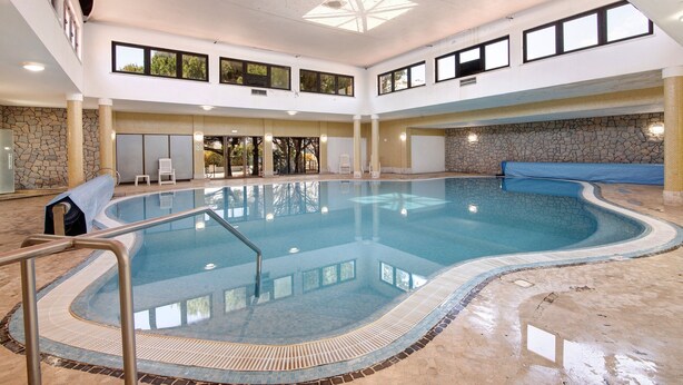 Ein überdachter Innenpool mit Steinwand und hoher Decke mit Oberlichtern.