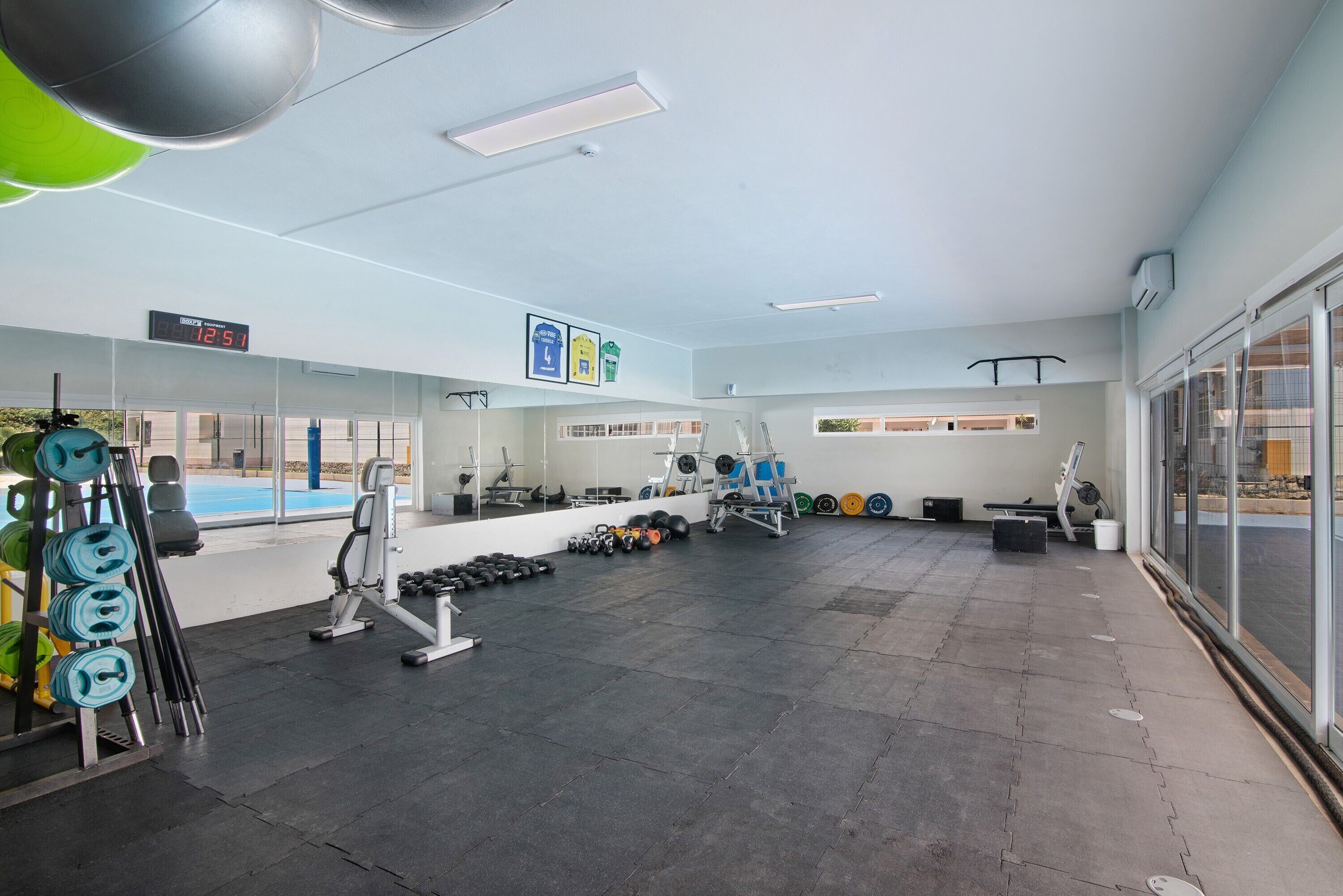 Ein Fitnessraum mit Trainingsgeräten, einer digitalen Uhr und großen Fenstern.