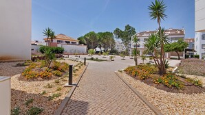 Ein gepflasterter Weg führt zu einer Wohngegend mit Gebäuden, Bäumen und blauem Himmel.