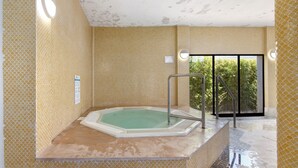 Ein Wellnessbereich mit Whirlpool, gefliesten Wänden und einer Glastür, die nach draußen führt.