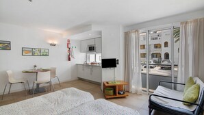 Ein Hotelzimmer mit Bett, Schreibtisch mit Stuhl, Küchenzeile, Fernseher und einem Balkon mit Straßenblick.