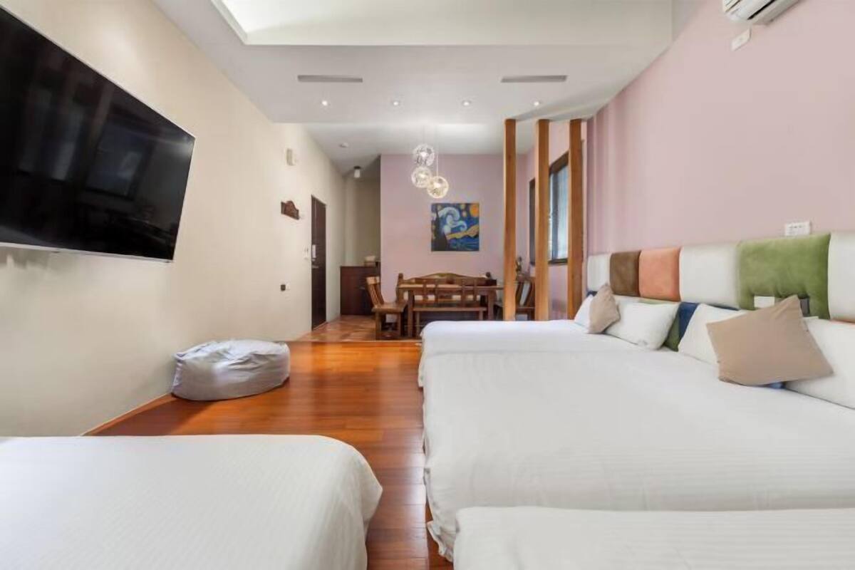 A hotel room with two beds, a TV, a dining area, and a painting on the wall.