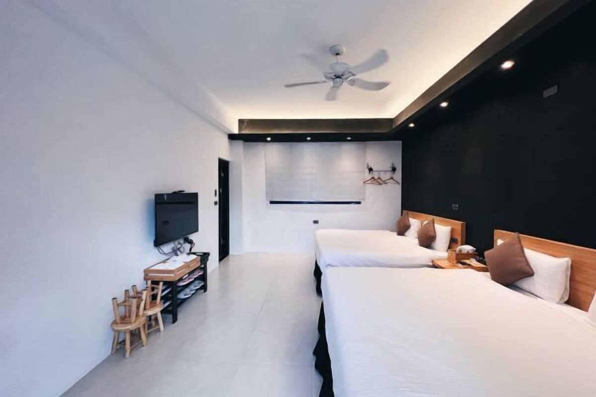 A modern hotel room with two beds, a TV, a desk with chairs, and a ceiling fan.