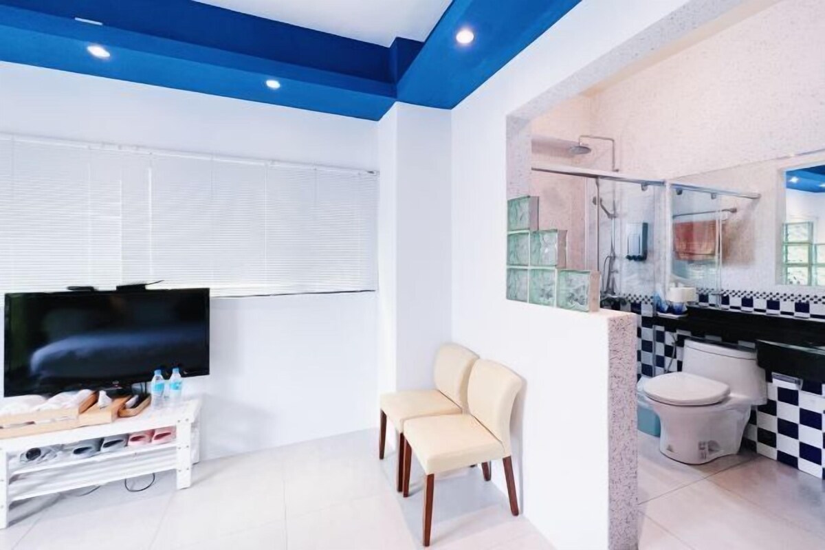 A modern bathroom with a shower, toilet, and sink. There is a TV and a seating area with a chair.