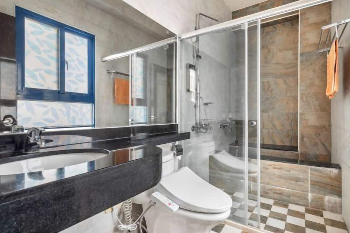 A modern bathroom with a glass-enclosed shower, a black countertop sink, and a white toilet.